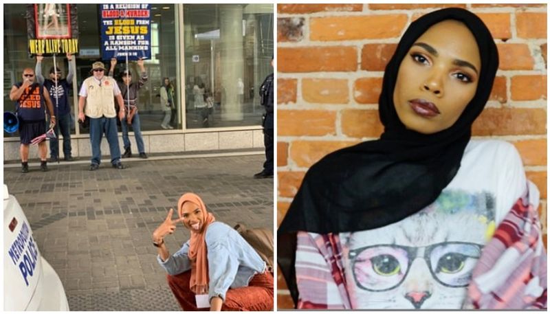 woman takes smiling photo infront of Islamophobic protesters