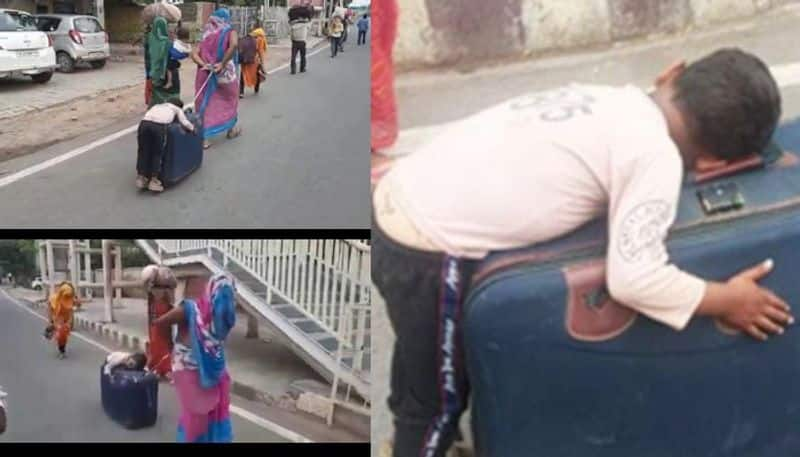 boy sleeps on suitcase wheeled by mother