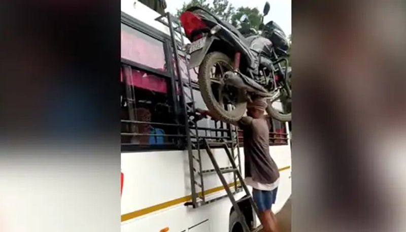 man carries heavy motorbike on his head and climbs a ladder 