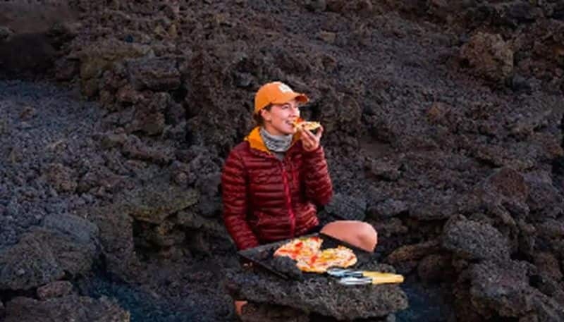 woman traveler eats pizza that cooked in active volcano hyp