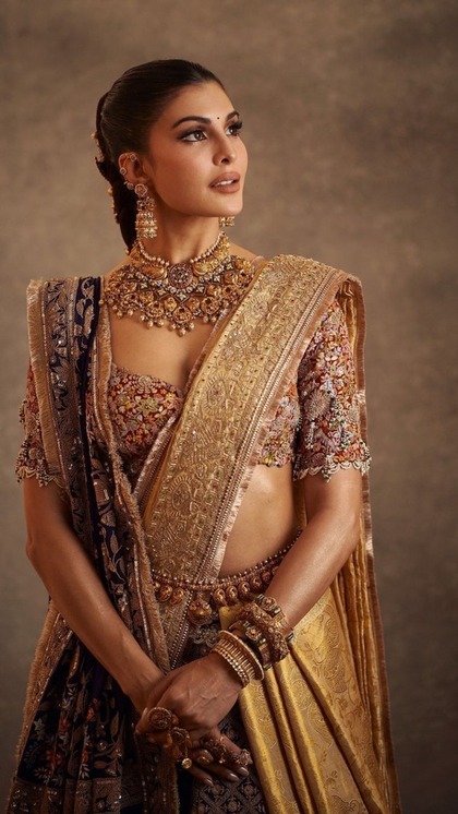 <p>गोल्ड-पर्पल साउंथ इंडियन ट्रेडिशनल साड़ी में जैकलीन फर्नांडीज कमाल लग रही हैं। उन्होंने आउटफिट को खास बनाती हुए स्वीटहार्ट नेकलाइन पर मल्टी कलर ब्लाउज हैवी नेकलेस स्टाइल पहना है। </p>
