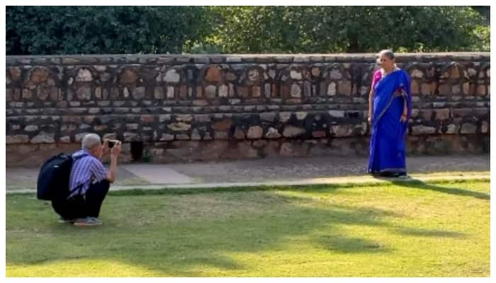 Video of an elderly man sitting on the ground and taking photos for the best picture of his wife 