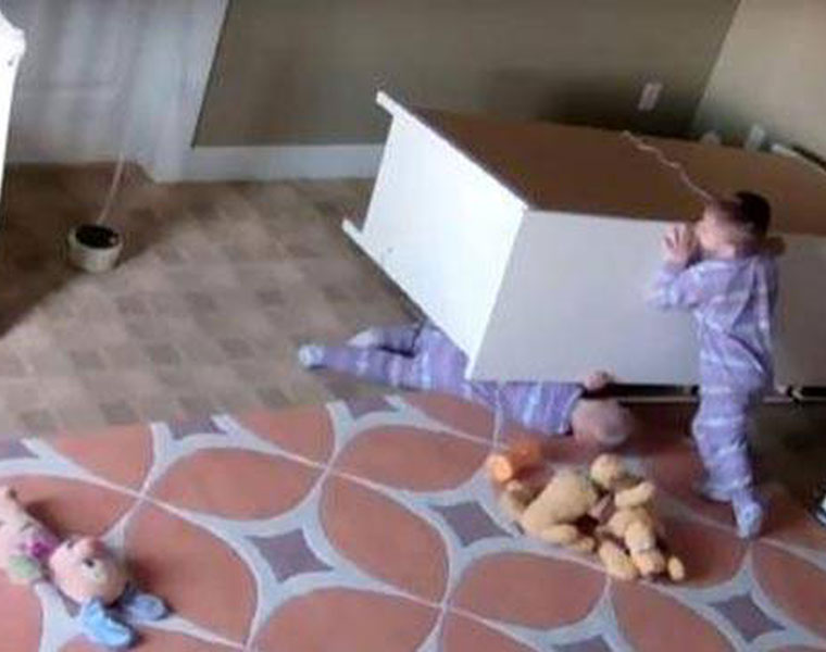 2 year old tries to lift fallen dresser off twin brother